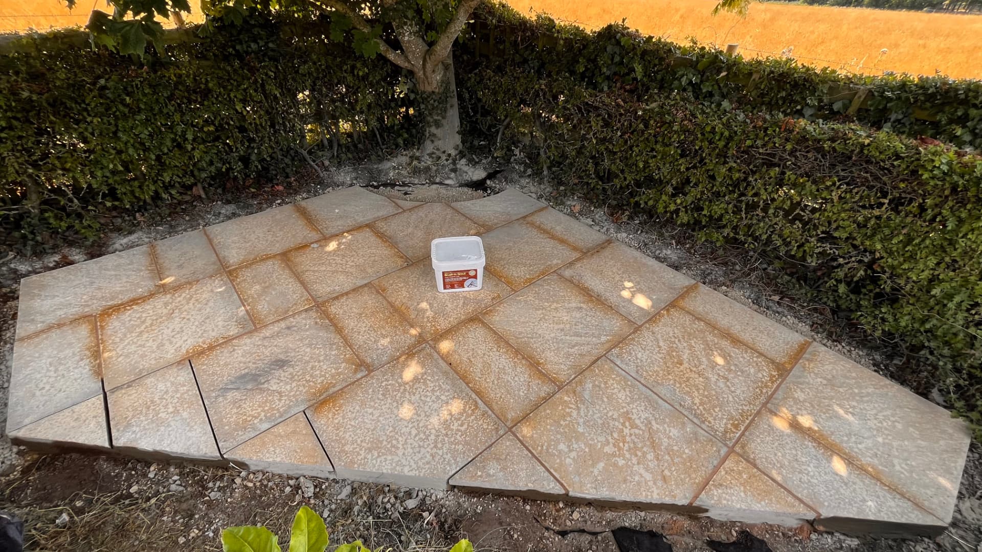 Newly laid sandstone patio in a herringbone-style layout beside a hedge